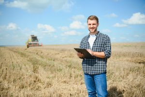 Handsome,farmer,with,tablet,standing,in,front,of,combine,harvester